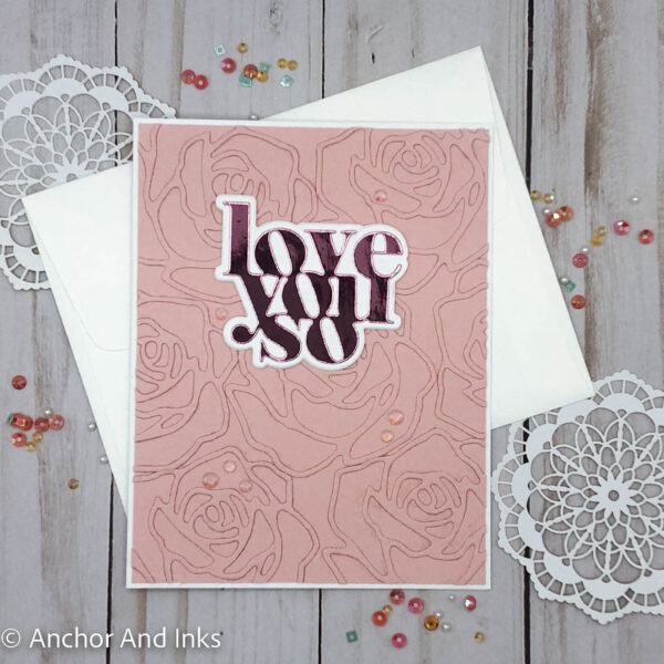 pink valentine card with die cut roses background and pink metallic wording that says love you so